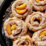 Peach Cobbler Cinnamon Rolls drizzled with icing on a plate