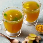 Bone Broth Turmeric Ginger served in clear glass mugs with fresh ginger root and turmeric powder on the side, showing a golden nourishing broth.