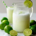 Creamy Brazilian lemonade in a glass pitcher with fresh limes and ice