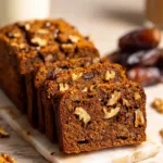 Sliced date walnut loaf cake showing dark moist crumb with walnut pieces on a marble board