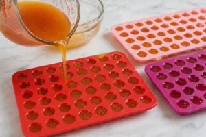 Apple cider vinegar gummy mixture being poured into red silicone molds. apple cider vinegar gummies recipe for weight loss