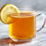 Bariatric gelatin recipe for weight loss in a clear glass mug with lemon slice on a light marble surface