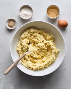 Cauliflower pizza crust dough mixed with egg and parmesan in a white bowl , cauliflower pizza crust